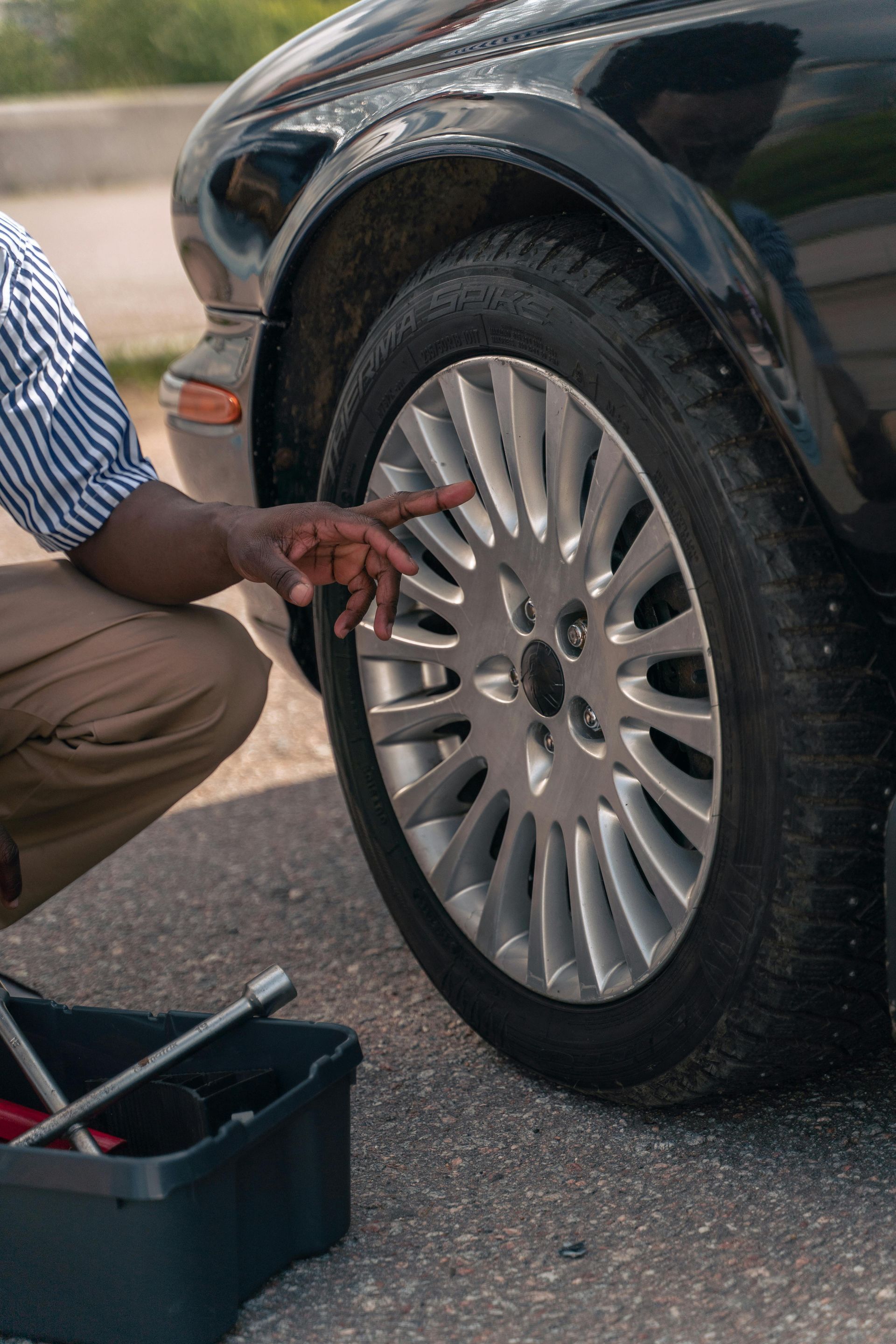 A man is changing a tire on a black car.
