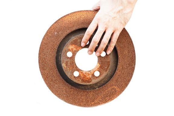 A person is touching a rusty brake disc with their hand.