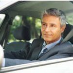 A man in a suit and tie is driving a car.