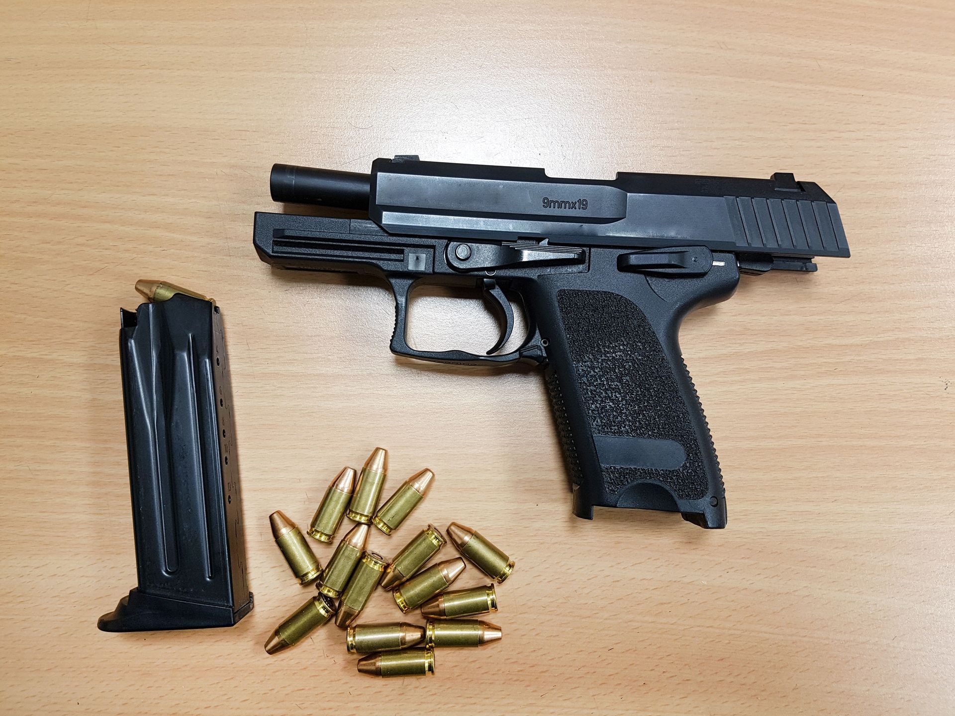 Black handgun with open slide, magazine, and ammunition on a wooden surface. Black handgun with open slide, magazine, and ammunition on a wooden surface.