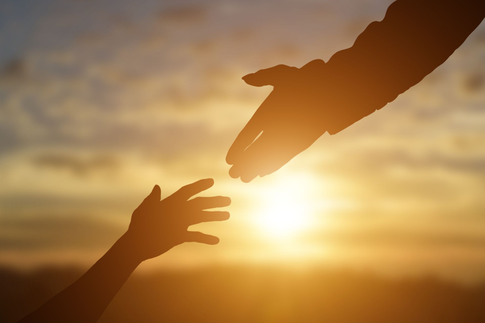 Two hands reaching toward each other at sunset, silhouetted against a golden sky
