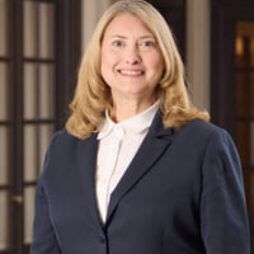 Professional woman in a navy blazer and white blouse, smiling in an office setting.