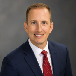 Smiling professional in navy suit and red tie against a gray studio background