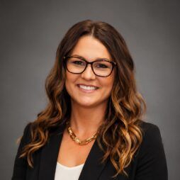 Smiling professional in black blazer and glasses against a gray studio background