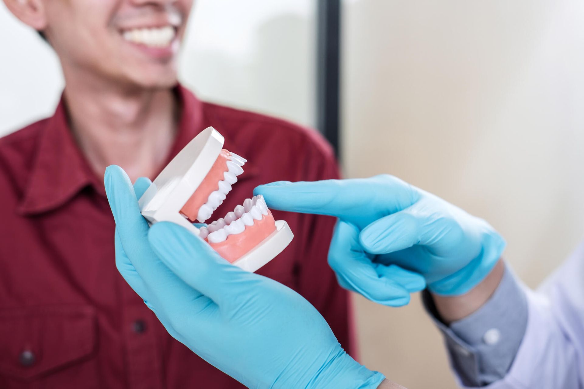 Dentist in blue gloves showing a dental model to a smiling patient during an exam