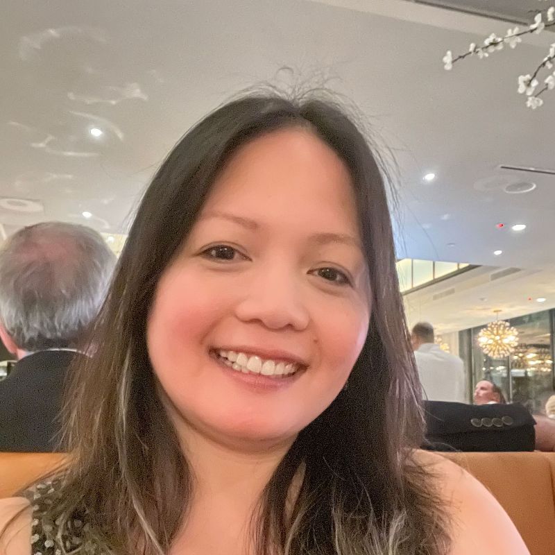 Smiling person in a tan booth at a restaurant, with warm lighting and blurred diners in the background.