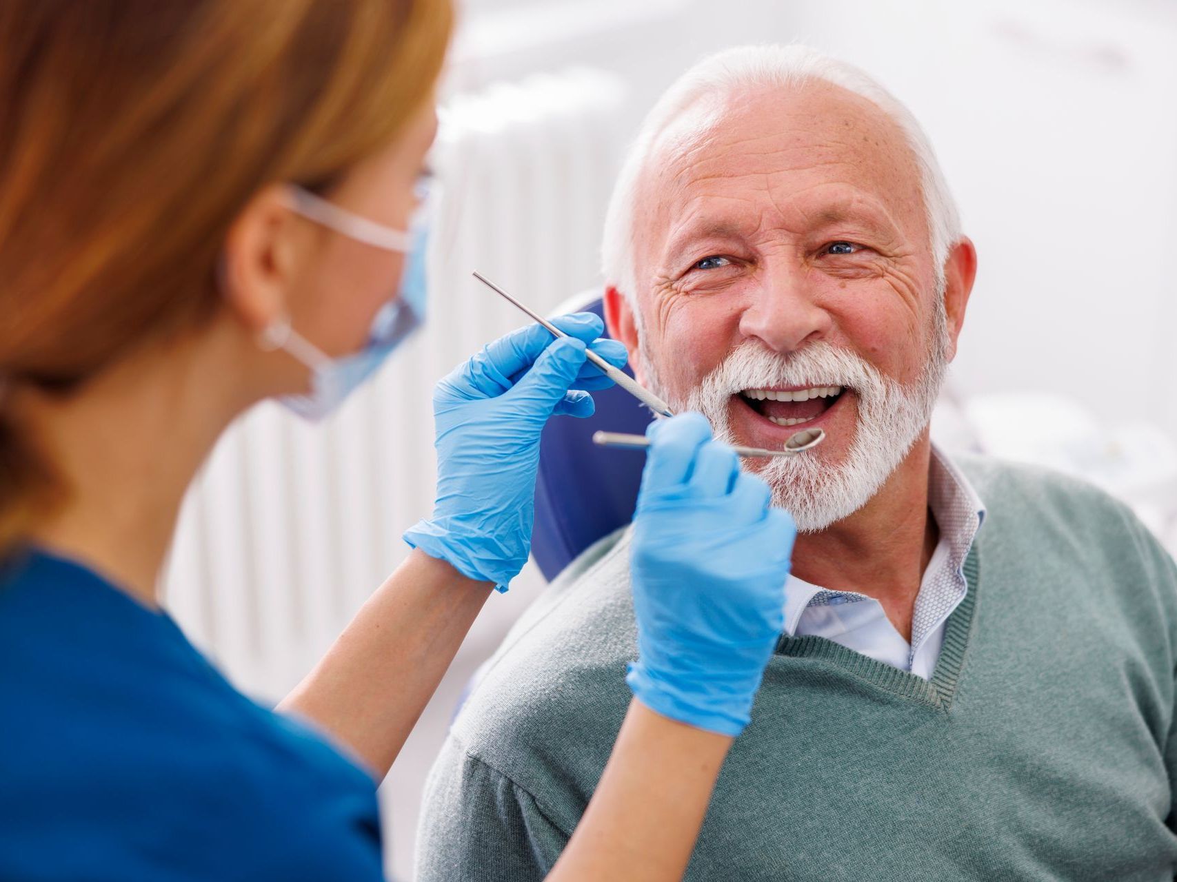 Dentist examining an older man's teeth with a mirror and tool in a clinic