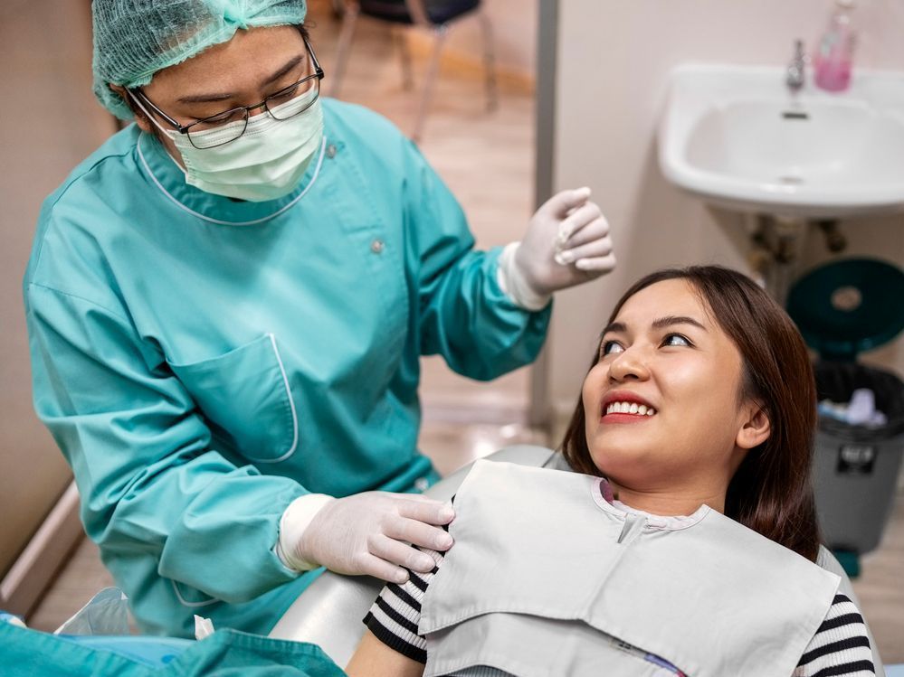 Dentist in teal scrubs examines a smiling patient in a dental chair