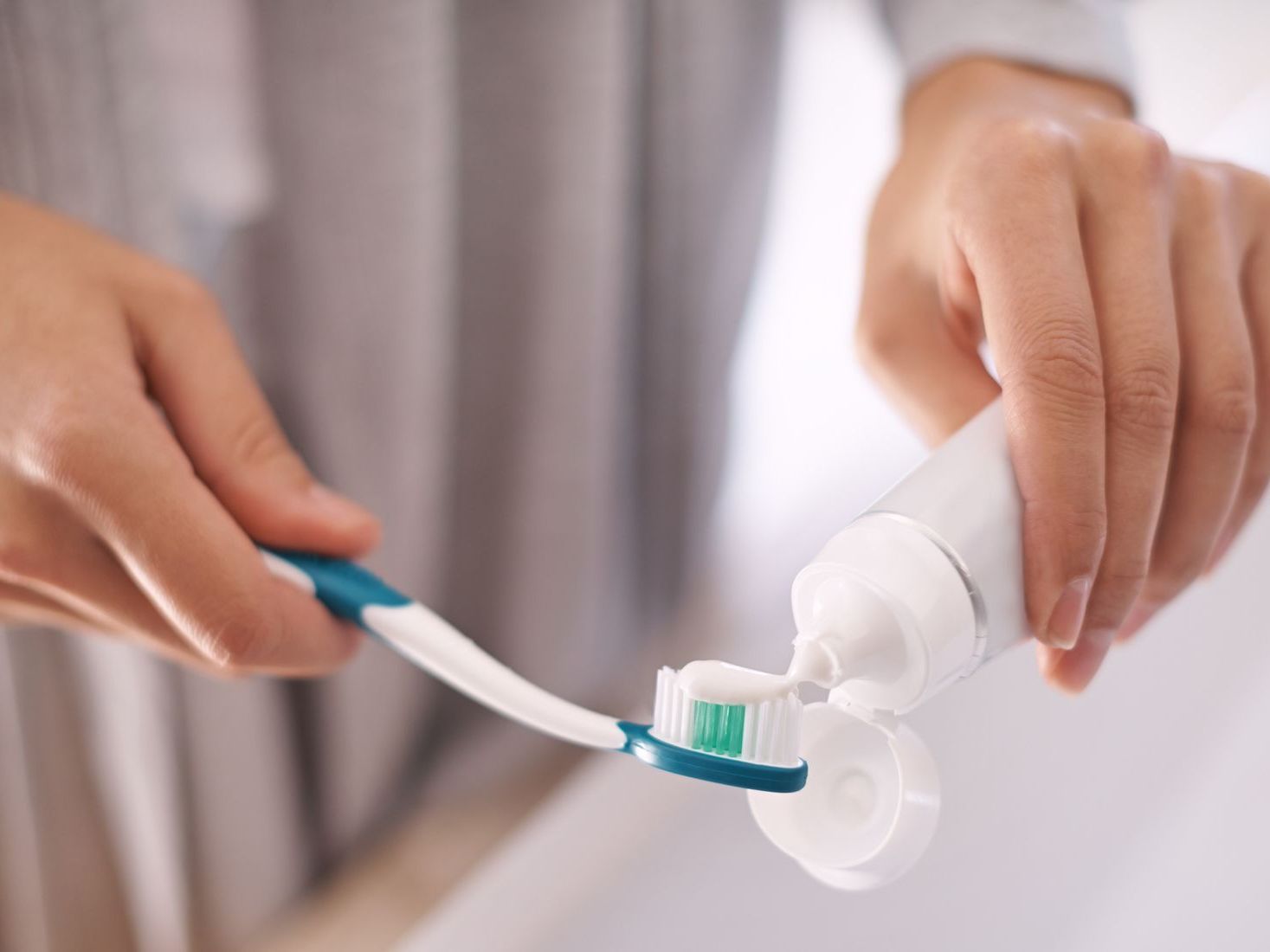 Hands brushing toothpaste onto a toothbrush near a toothpaste tube