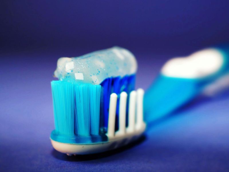Blue and white toothbrush with toothpaste foam on the bristles against a purple background