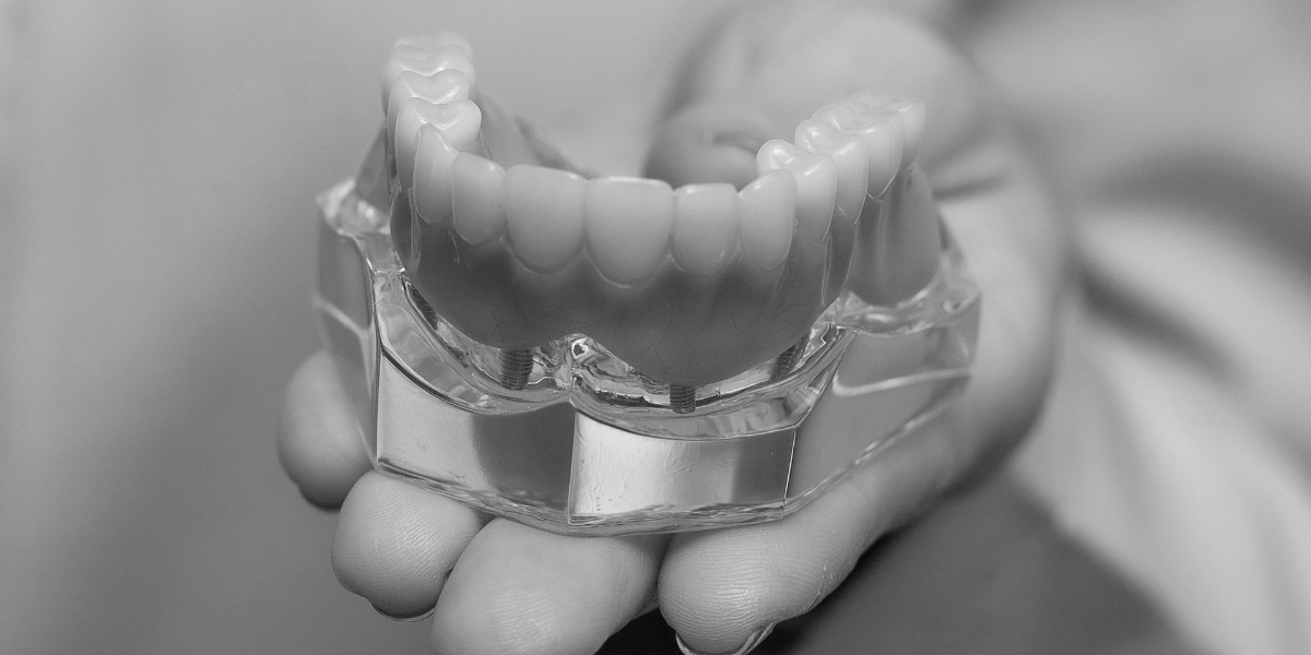 A hand holding a clear dental mold with white teeth on a gray background