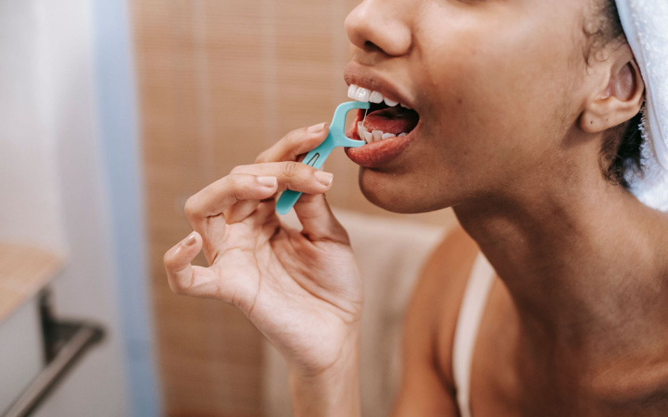 Person brushing teeth with a blue toothbrush in a bathroom mirror
