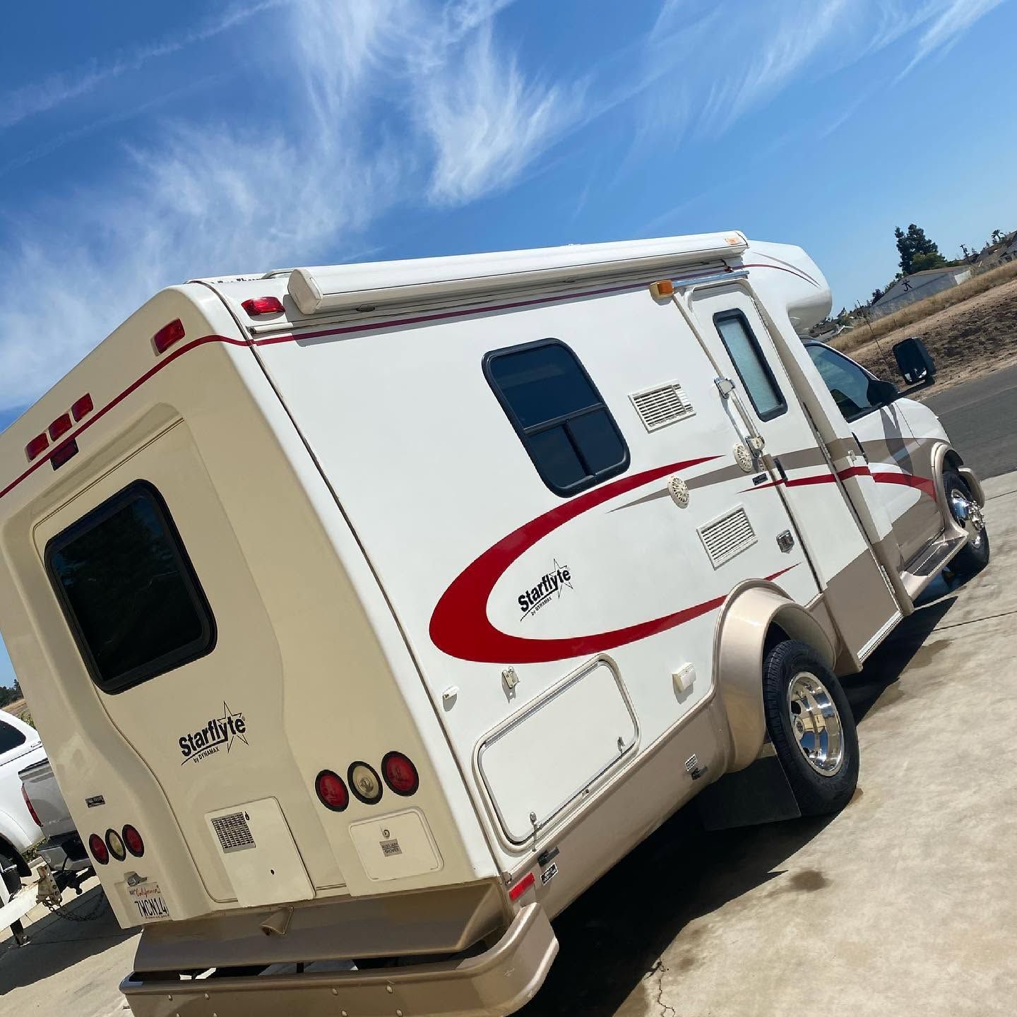 White RV with red stripe parked on a road under a blue sky