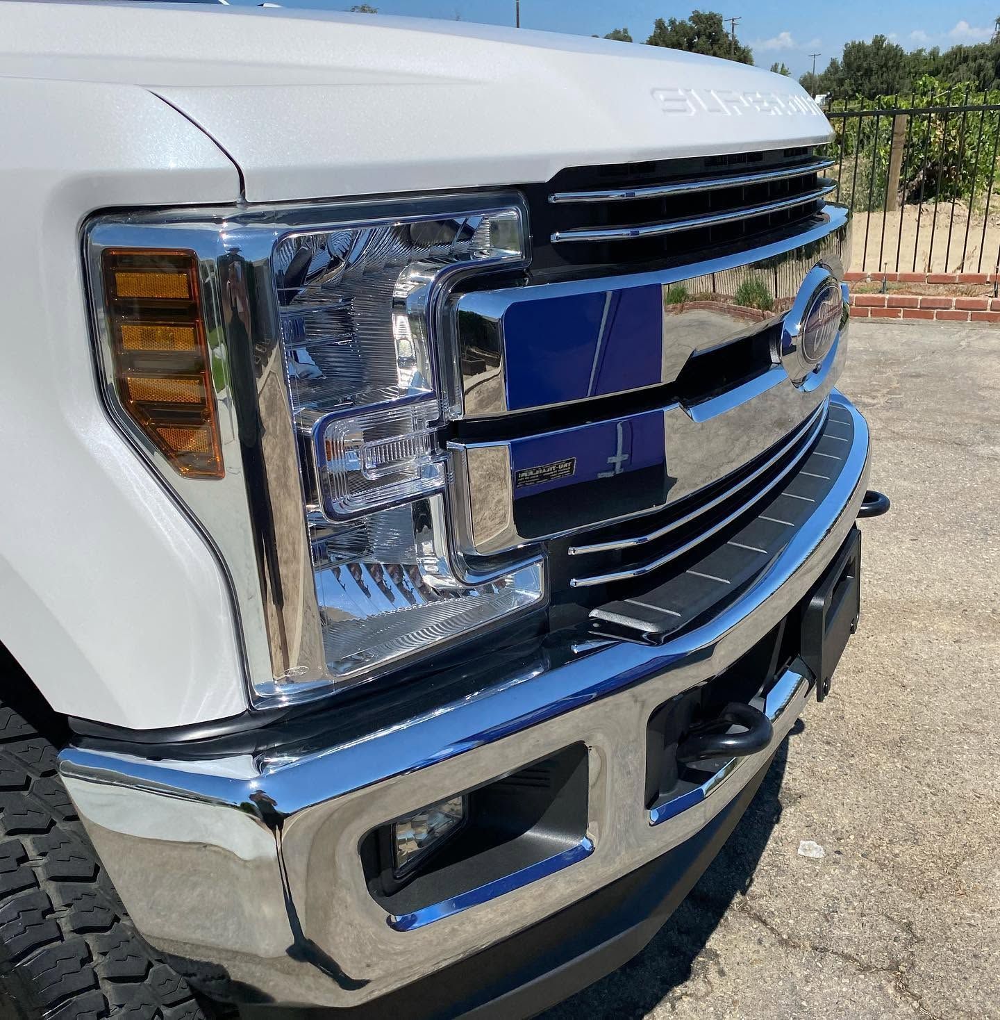 Close-up of a white pickup truck’s chrome front grille and bumper in a parking lot