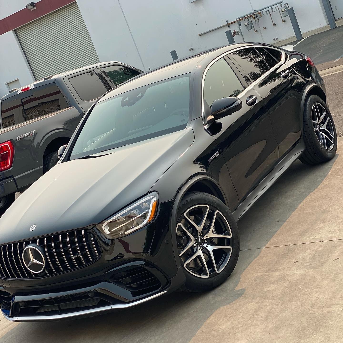Black Mercedes sedan parked outdoors beside a gray pickup truck in a lot