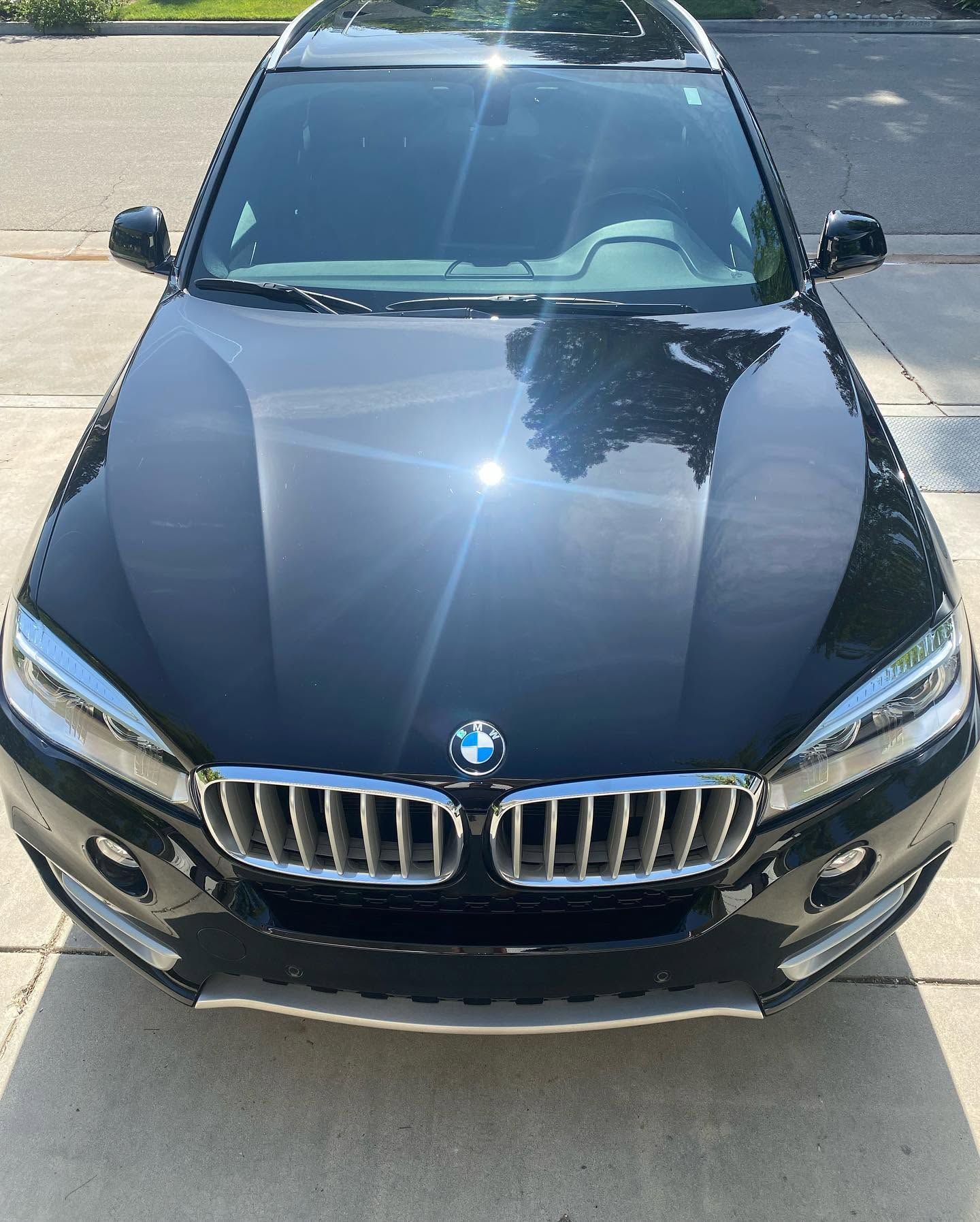 Black BMW sedan parked in a driveway, front view under bright sunlight.
