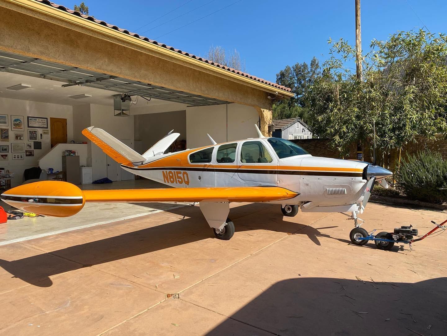 Small orange-and-white single-engine airplane parked on a driveway beside a house, with a propeller and tow bar.