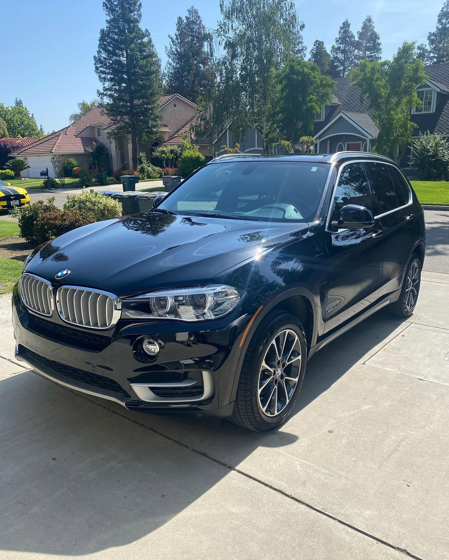 Black BMW SUV parked on a sunny suburban street with houses and trees in the background