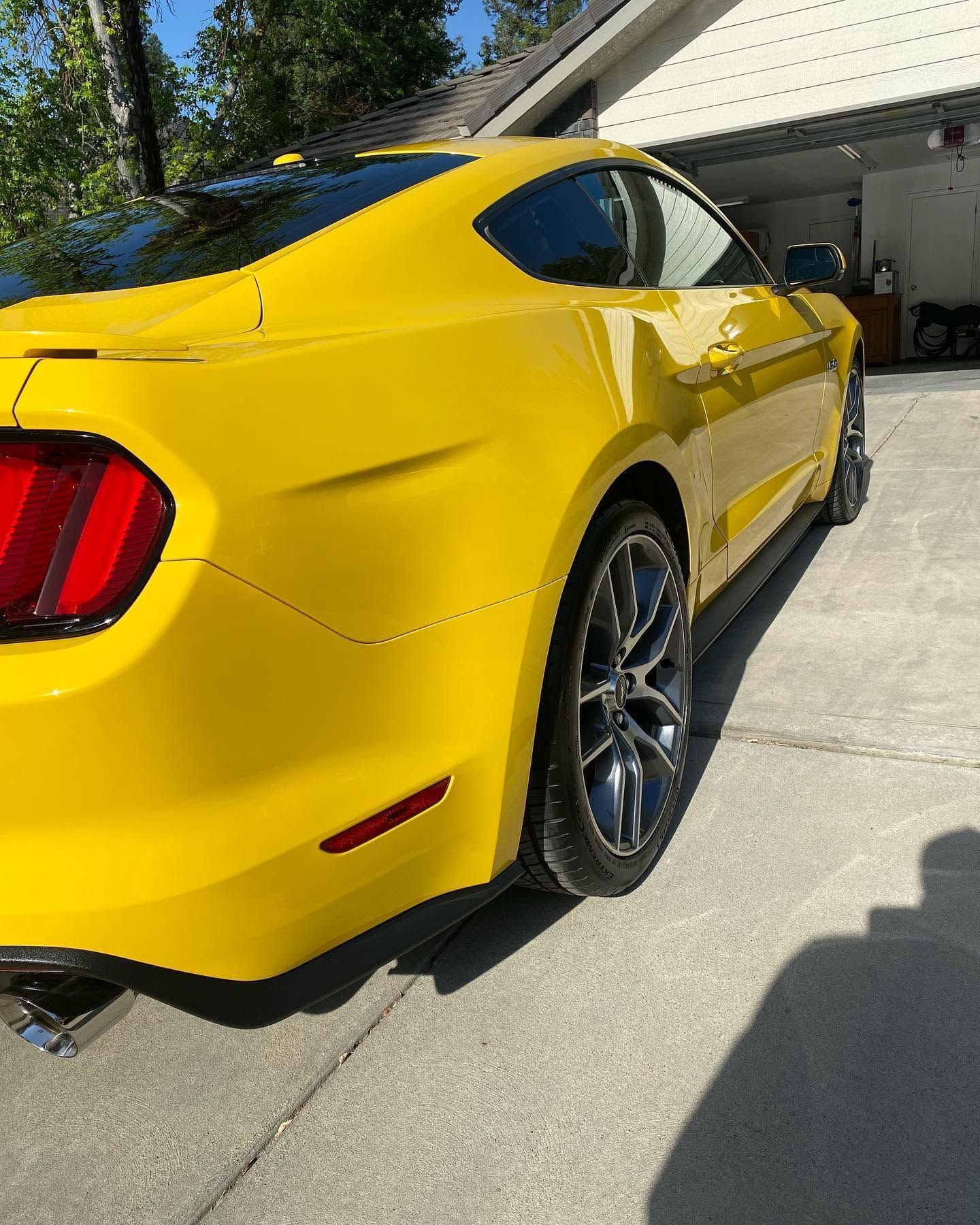 Yellow sports car parked in a driveway beside a garage on a sunny day.