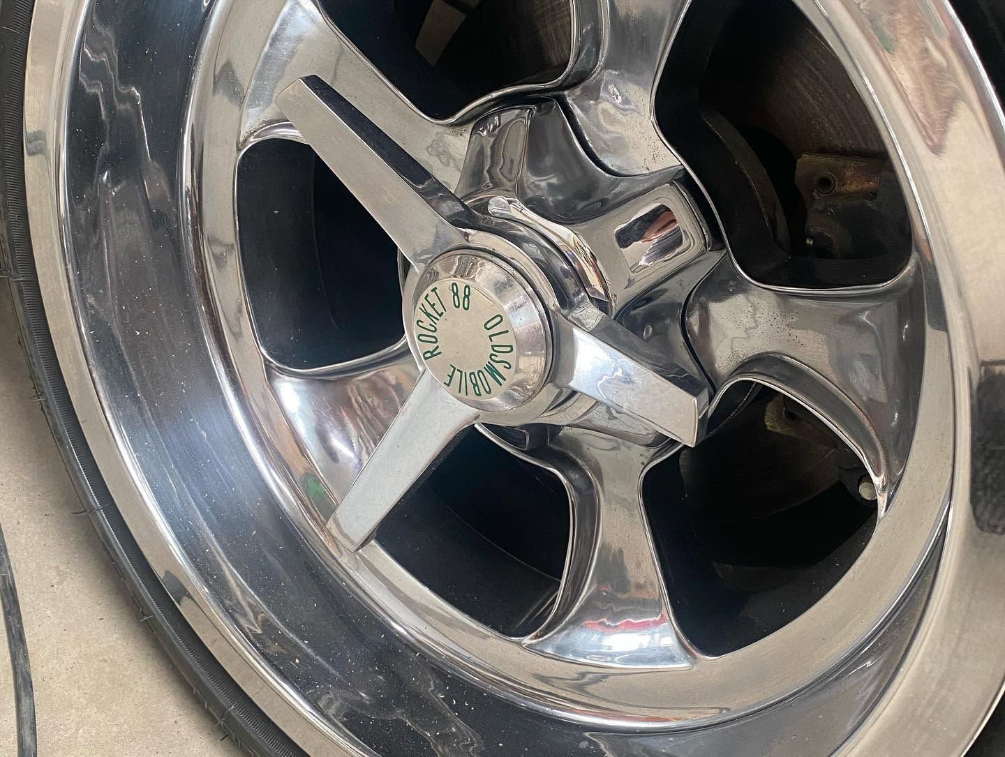 Close-up of a chrome car wheel rim with five spokes and a center cap, slightly dusty.