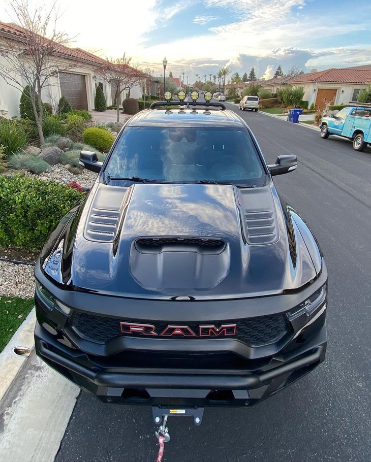 Black RAM truck parked on a suburban street with houses and another car nearby.