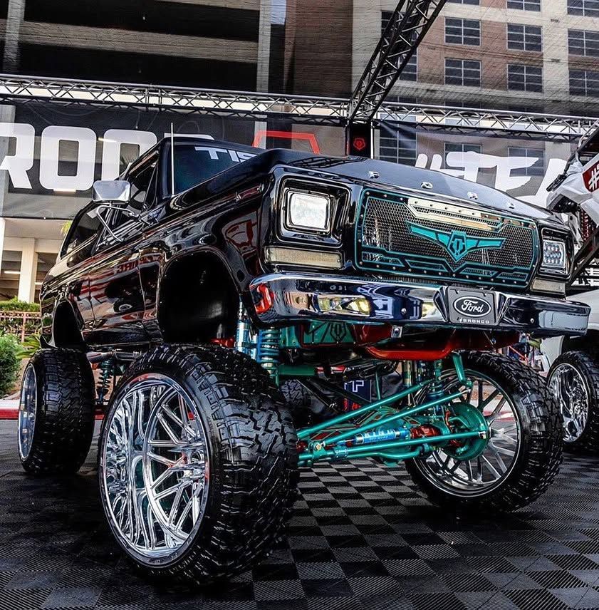 Custom lifted black truck with chrome rims and turquoise suspension at an indoor car show