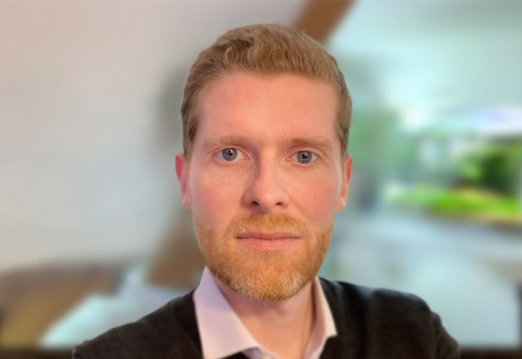 A man with a beard is wearing a black sweater and a white shirt.
