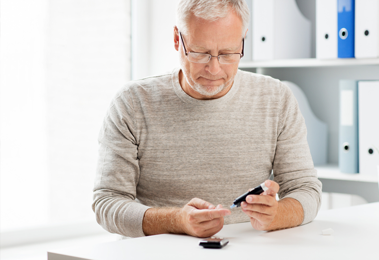 An older man is sitting at a table using a cell phone.