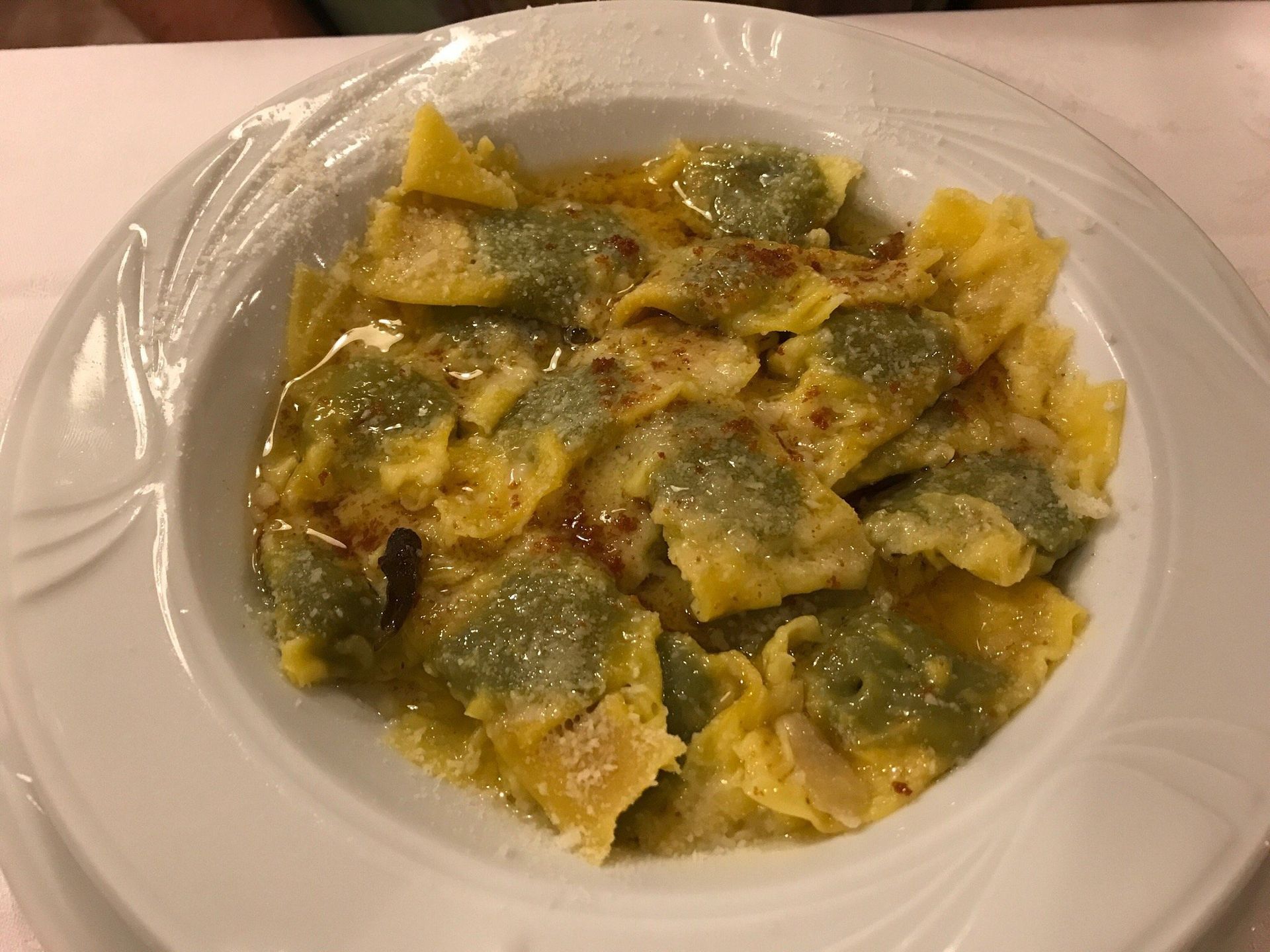 Piatto di ravioli verdi e gialli con salsa cremosa su un piatto bianco.