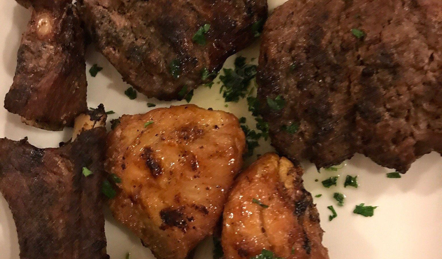 Piatti bianchi con pezzi di carne grigliata, crosticina dorata e guarnizione di prezzemolo tritato.