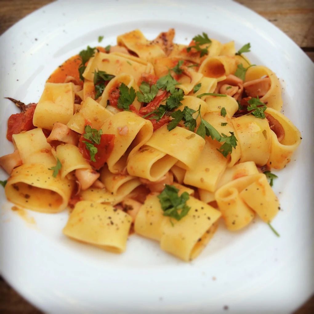 Tagliatelle di pasta al sugo di pomodoro, guarnite con erbe aromatiche tritate, servite su un piatto bianco.