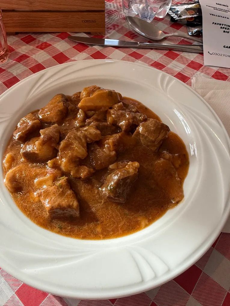 Un piatto di stufato denso in salsa arancione-marrone su una tovaglia a quadri rossi e bianchi.