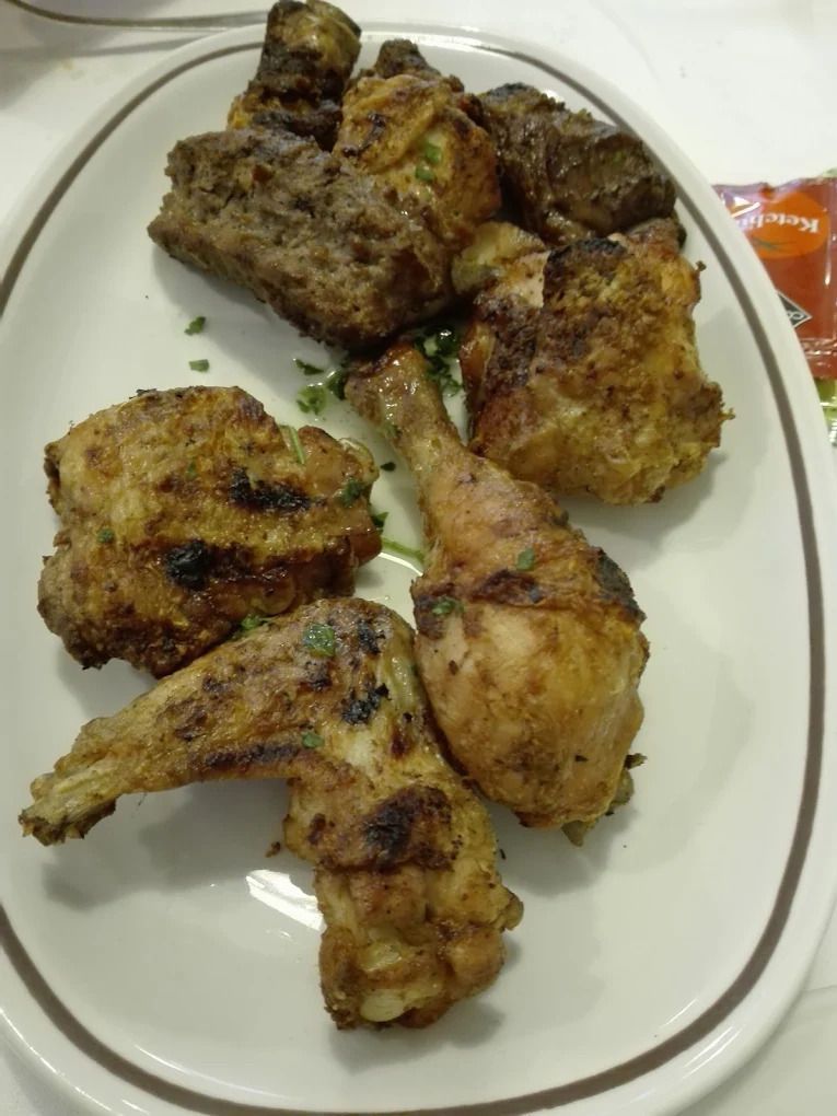 Piatto di pezzi di pollo grigliato su un piatto bianco, con condimento dorato e una bustina di guarnizione sul bordo.