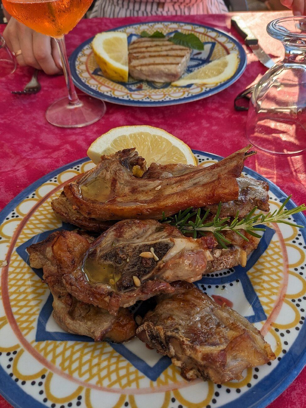 Pesce grigliato servito su una tovaglia colorata, con fette di limone e un bicchiere nelle vicinanze.