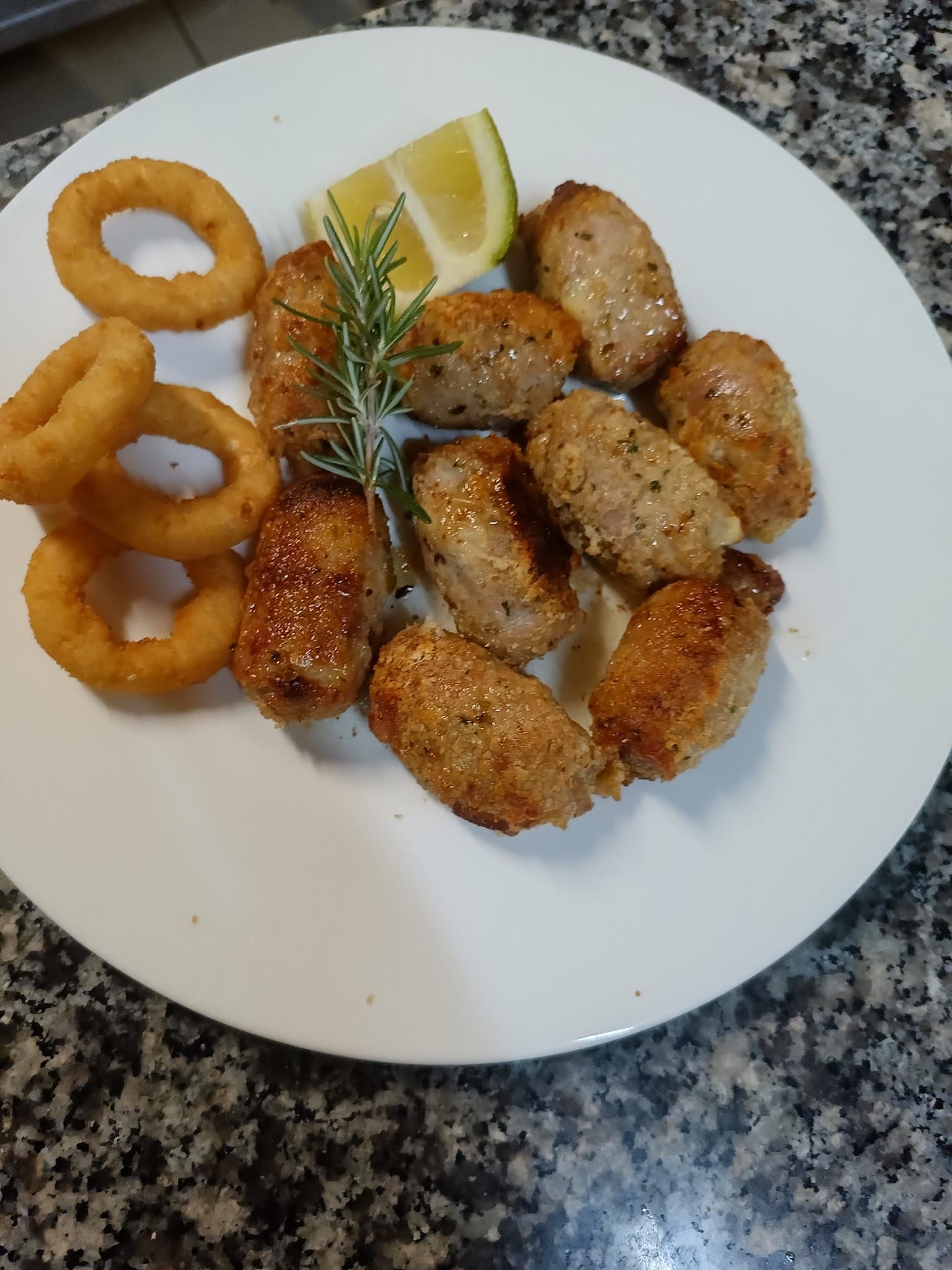 Piatto con frutti di mare fritti, anelli di cipolla e uno spicchio di limone su un piano di lavoro in granito.
