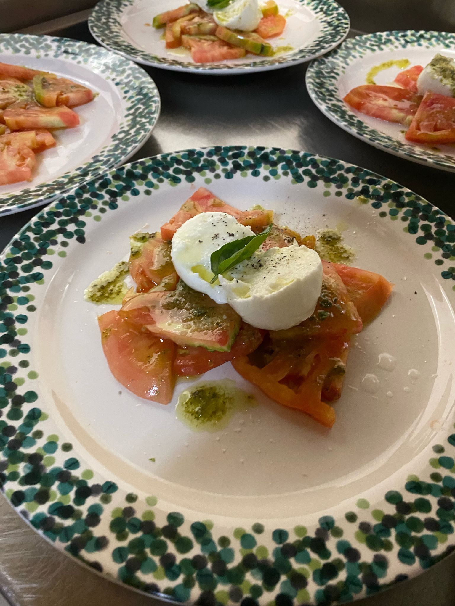Insalata di pomodori con burrata, olio al basilico e aceto balsamico servita su piatti decorati.