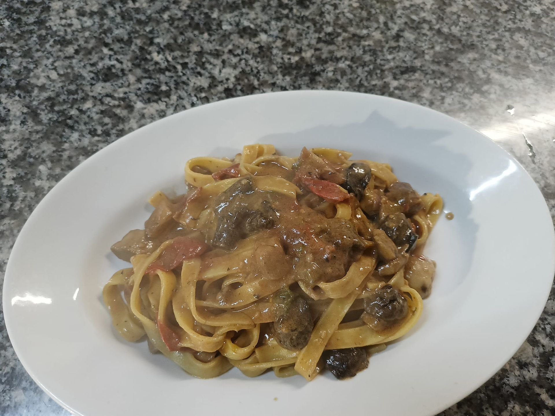 Piatto di pasta con sugo e verdure su un piatto bianco sul piano di lavoro