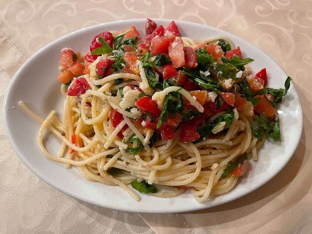Piatto di spaghetti conditi con pomodori a cubetti, basilico e formaggio grattugiato