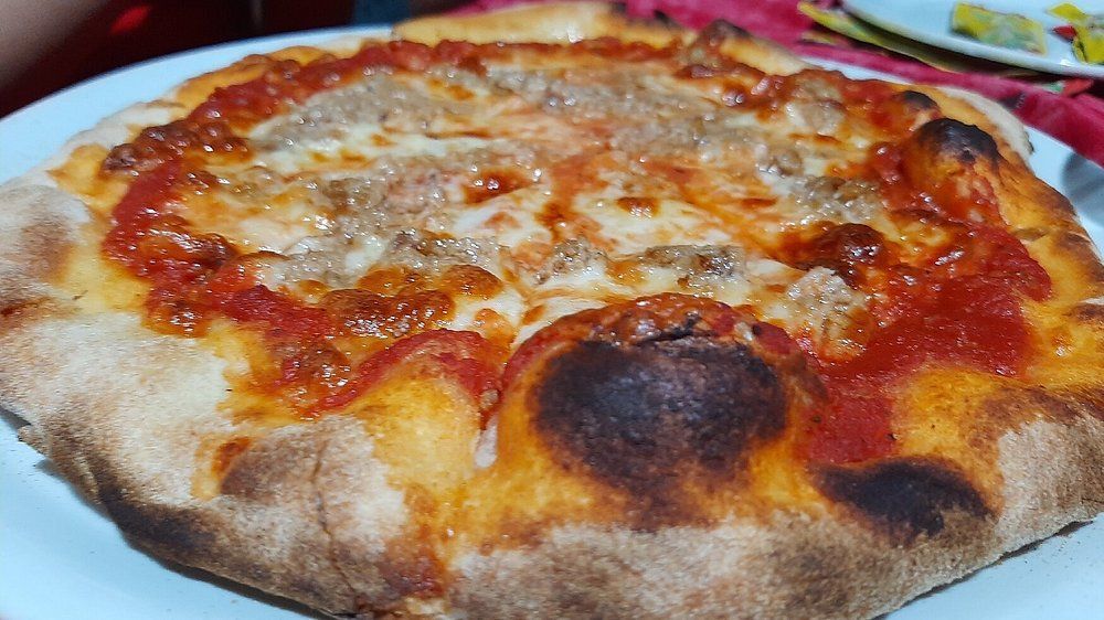 Primo piano di una pizza al formaggio con crosta dorata e salsa di pomodoro fusa su un piatto bianco.