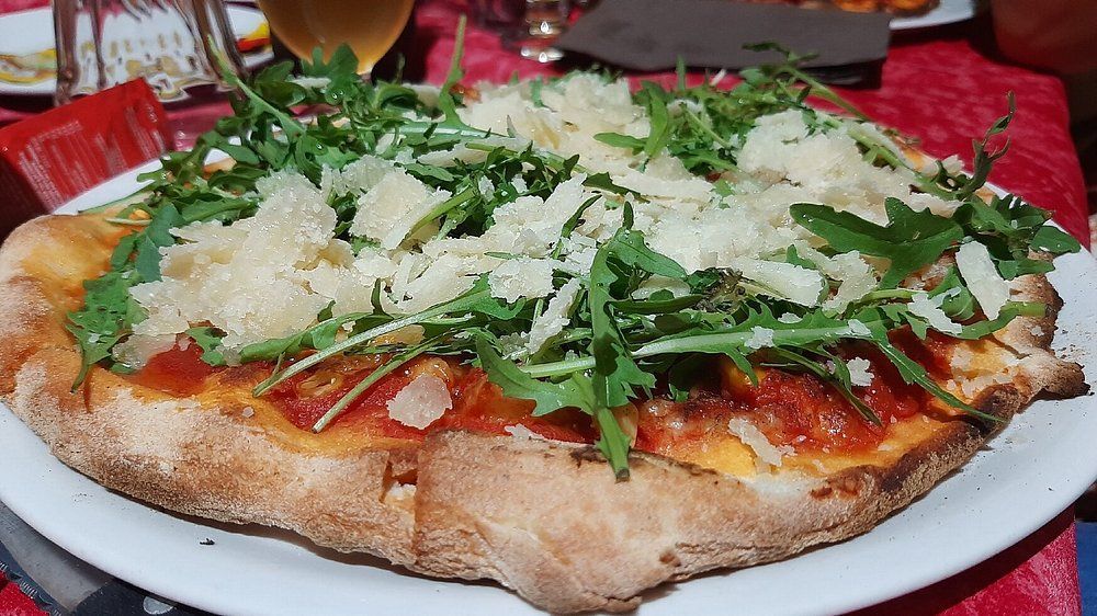 Pizza condita con rucola e formaggio grattugiato su un piatto bianco