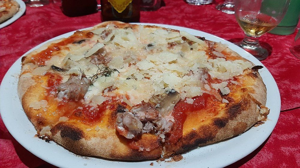 Pizza con formaggio e funghi su un piatto bianco, servita su una tovaglia rossa con bicchieri nelle vicinanze.