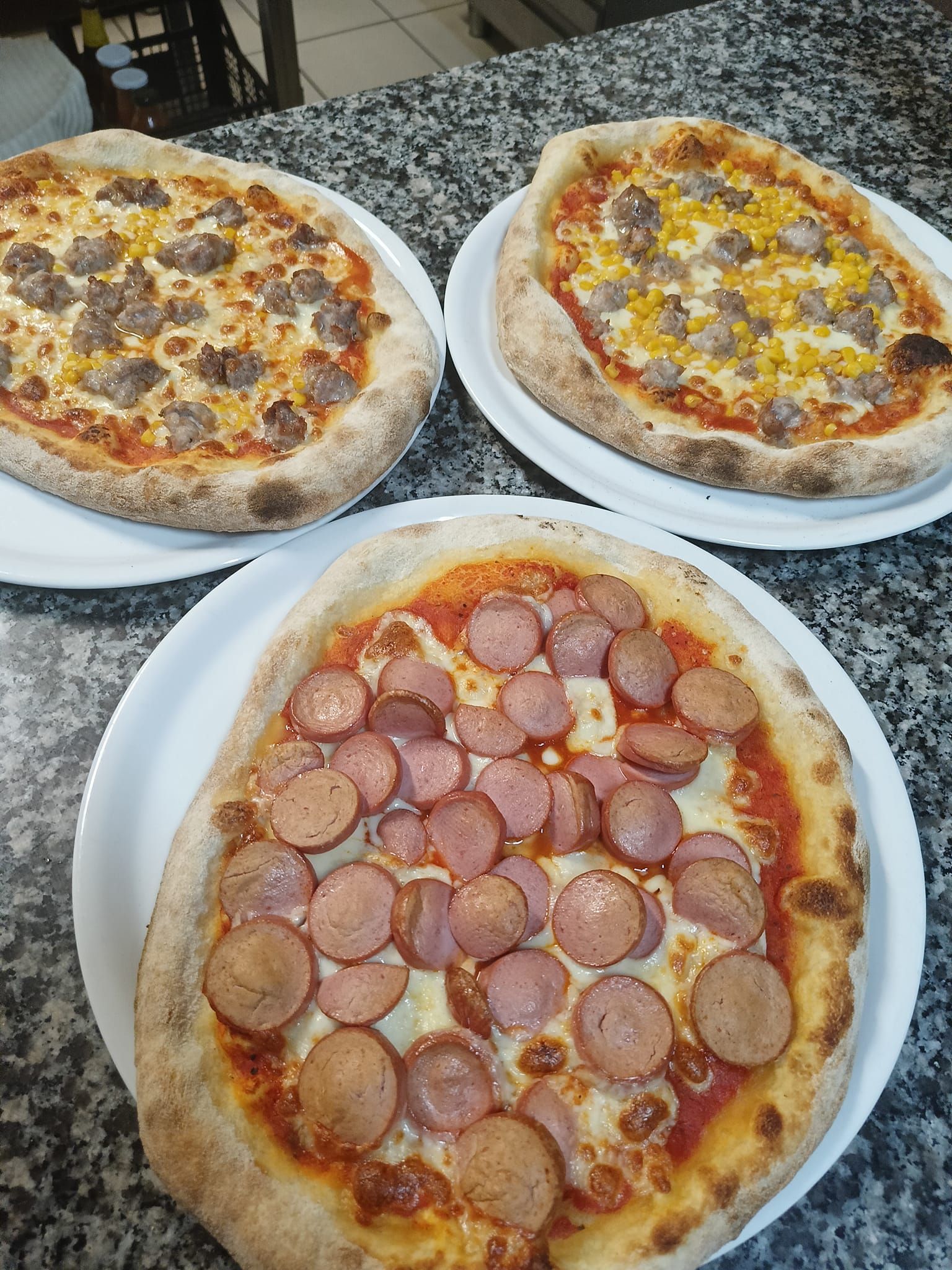 Tre pizze fatte in casa su piatti bianchi, tra cui una pizza al salame piccante in primo piano.