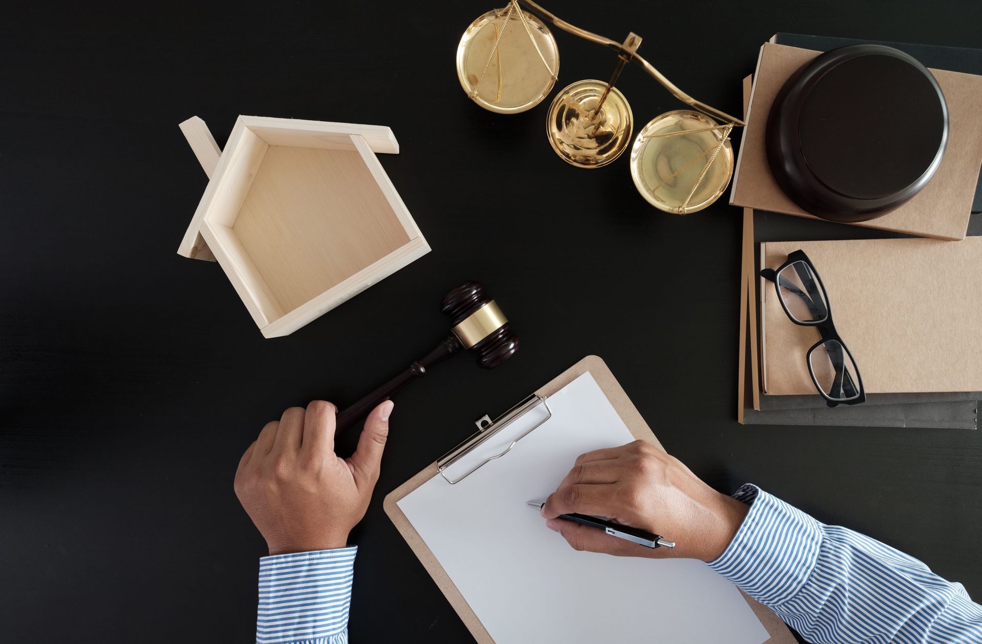 Top-down view of hands signing a document at a desk with a gavel, scales, papers, and glasses
