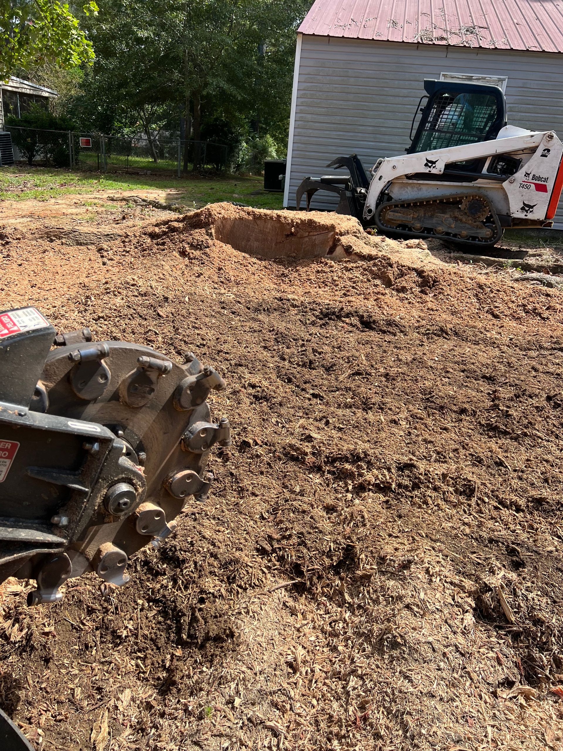 Skid steer loader moving a large mound of wood chips beside a building in a yard