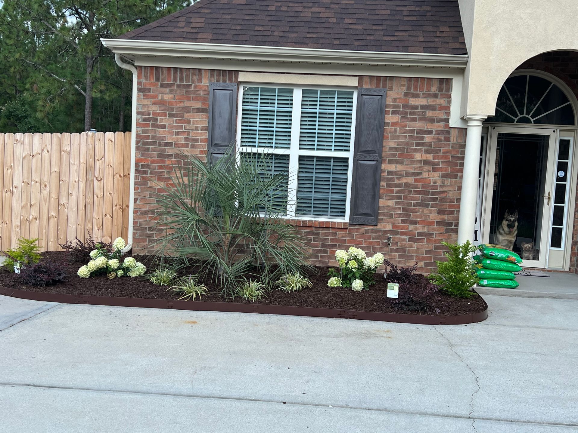 Brick house exterior with front window, flower bed, and open garage area