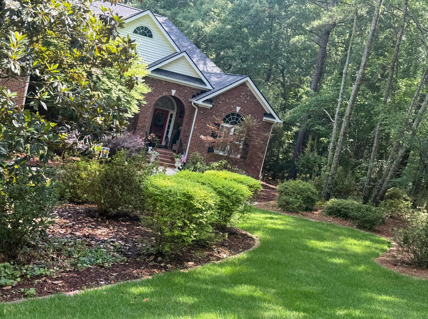 Brick house with arched porch surrounded by green lawn and trees in a wooded yard