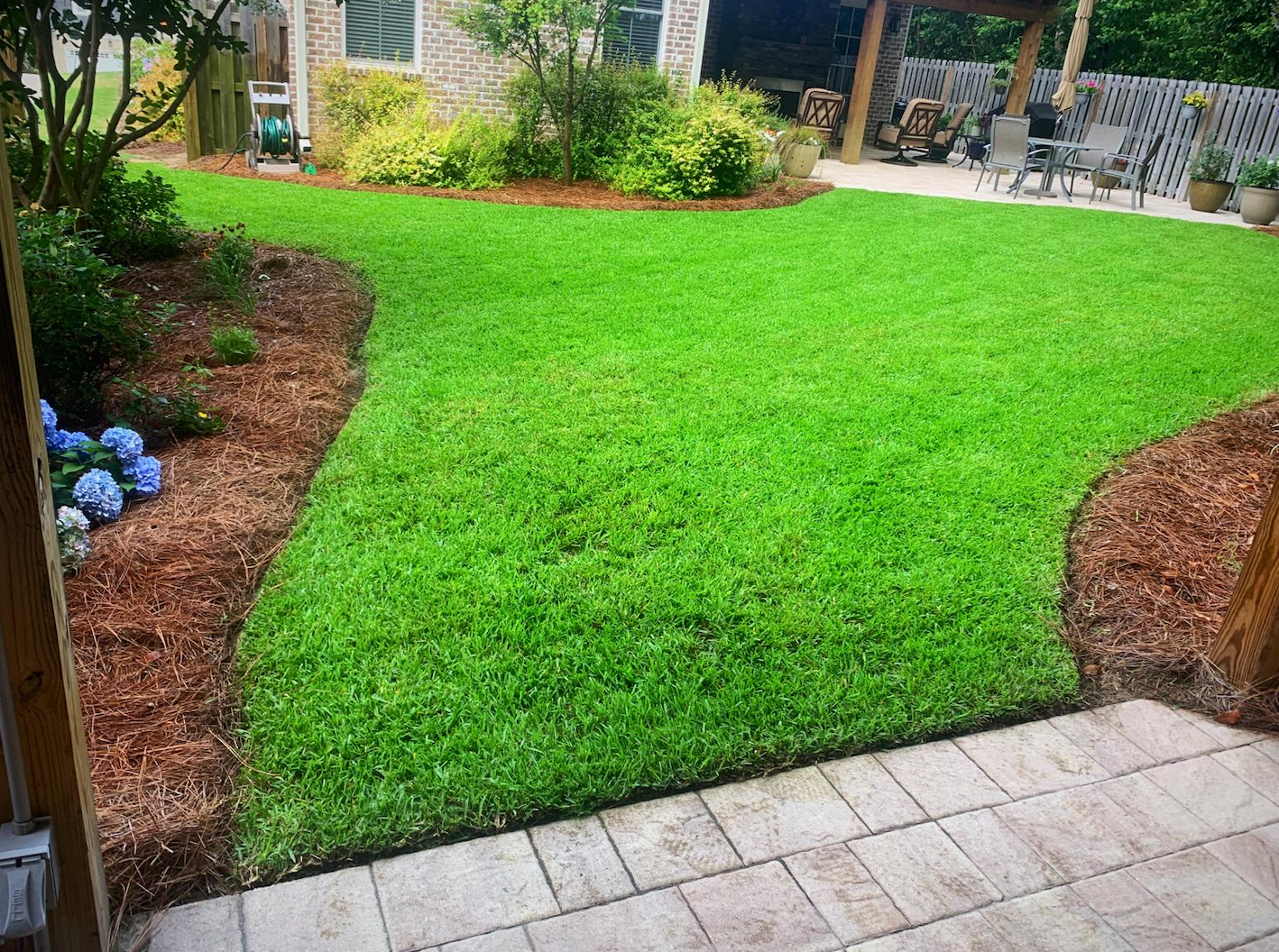 Bright green lawn bordered by mulch beds and a tiled patio in a backyard garden