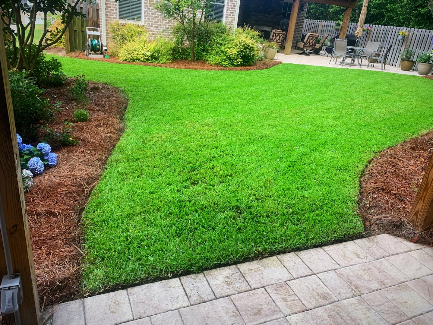 Small green backyard lawn bordered by mulched beds and a stone patio.