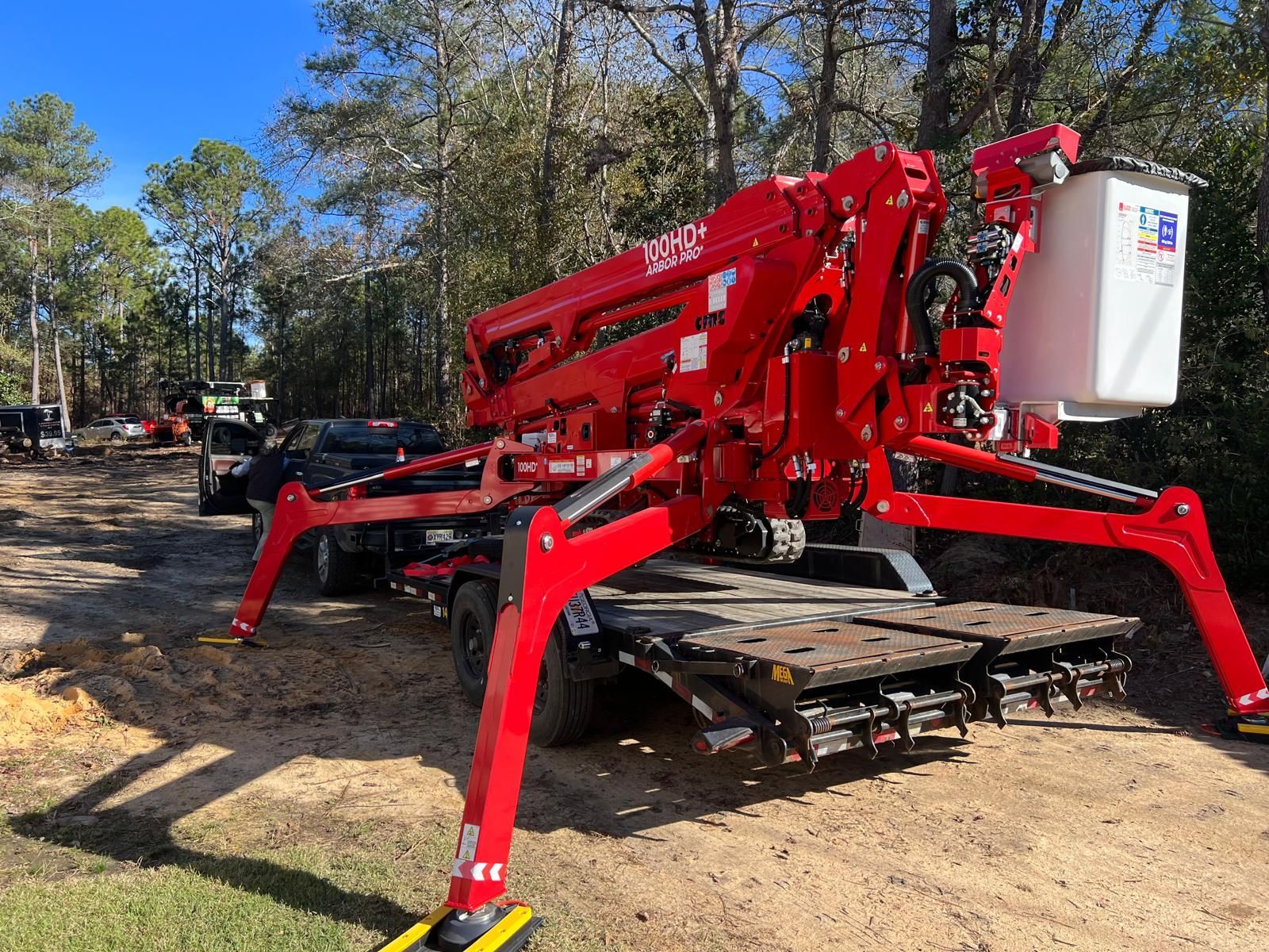 A bright orange skid steer with a black hydraulic claw attachment lifting a large tree stump in a grassy backyard.
