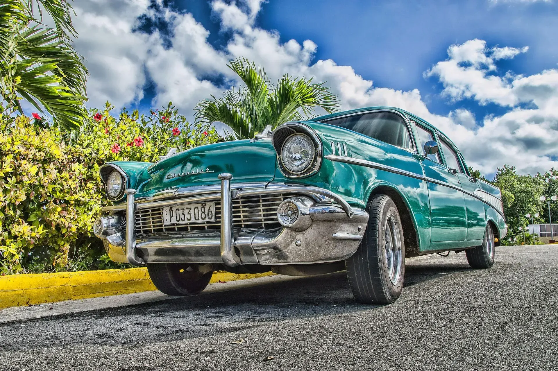 Teal vintage car parked on a cobblestone road under a sunny sky.